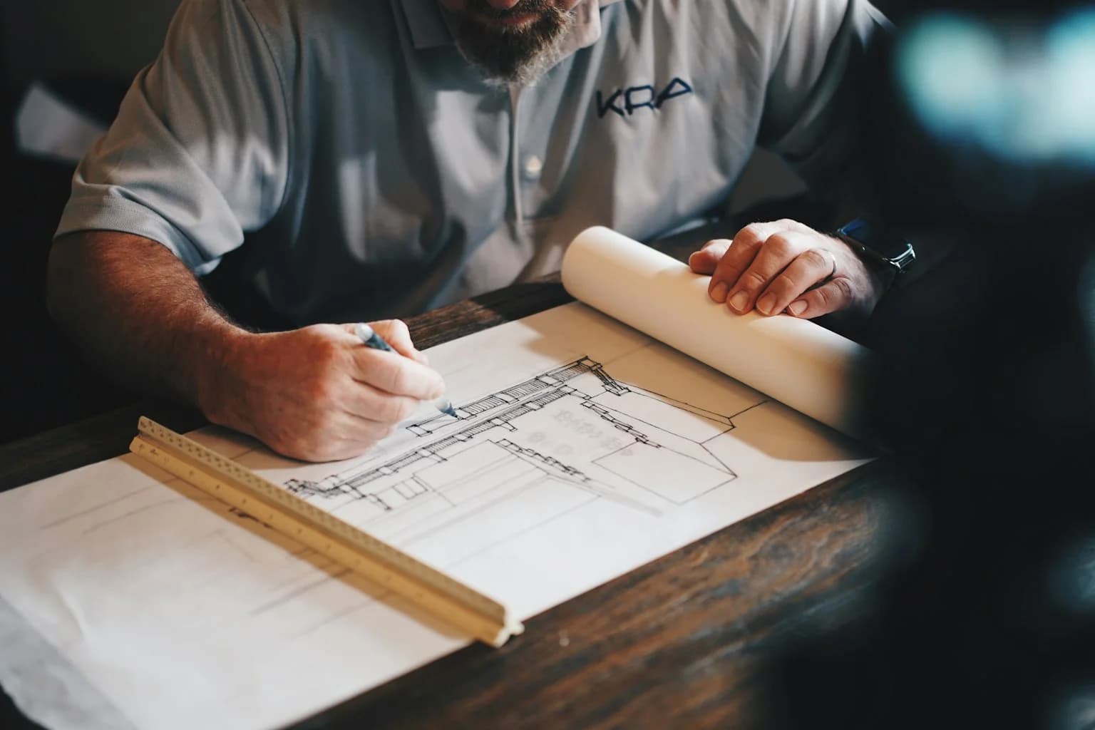 Architect using a pencil and ruler to work on a building drawing at a drafting desk